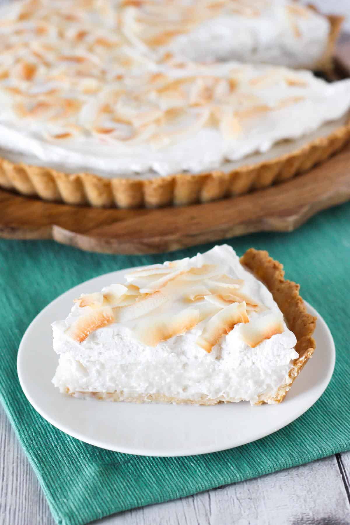 Slice of vegan coconut cream pie on plate with whole pie in background