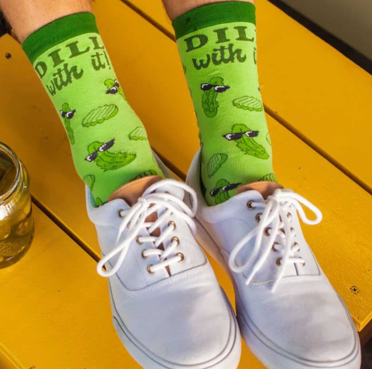 Feet wearing "Dill with it!" green pickle socks with white lace up shoes
